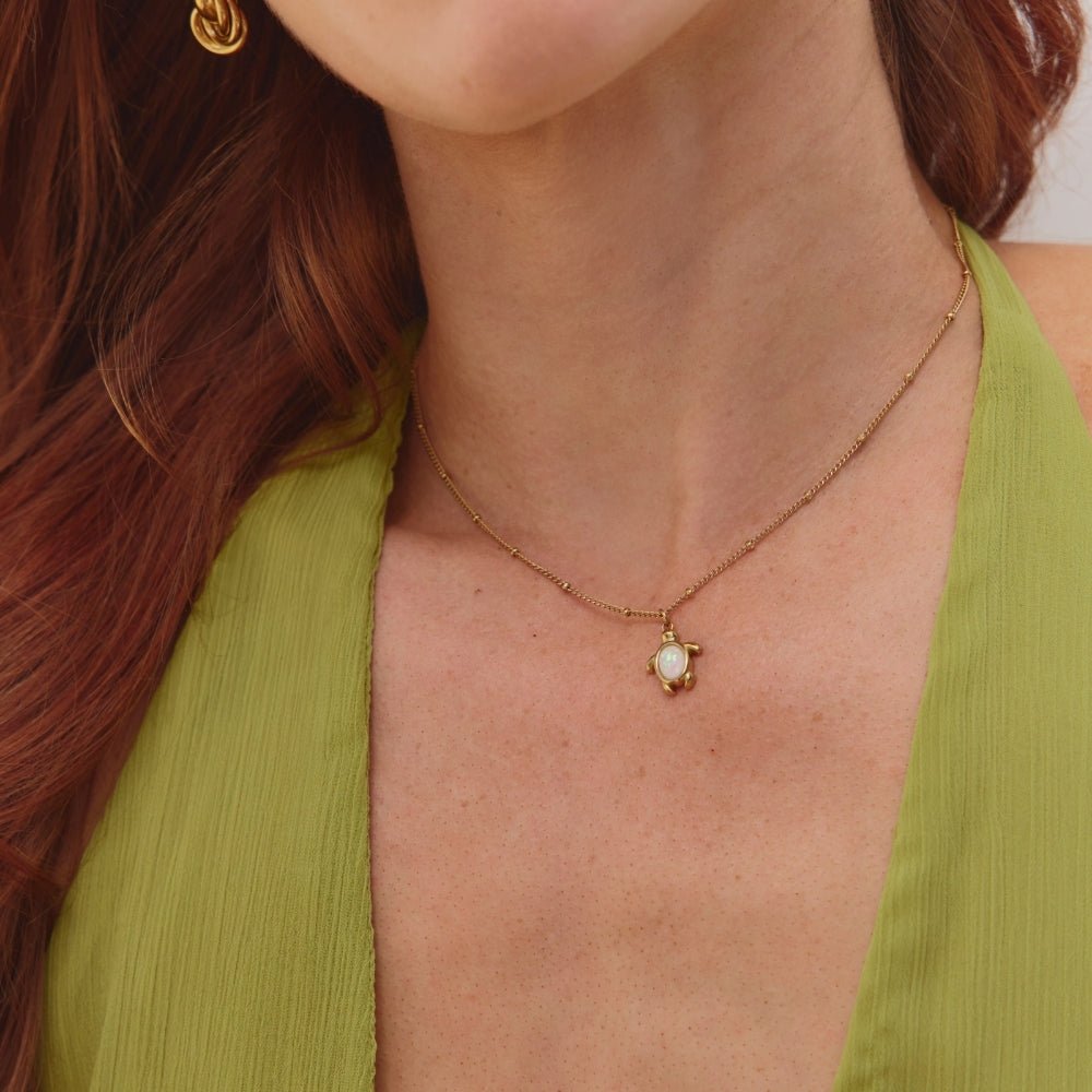 Opal Gold Turtle Pendant Necklace, worn on a model in a green top, with a gold chain and opal turtle